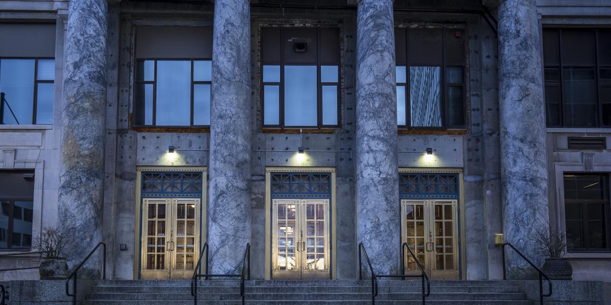 Marble columns and lit entry doors of the Alaska State Capitol in Juneau at dusk